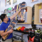Person working at a skate shop, hanging skateboards on the wall