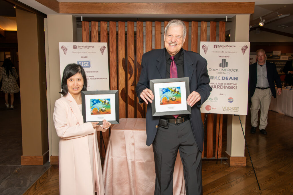 Two individuals smile while holding framed artwork