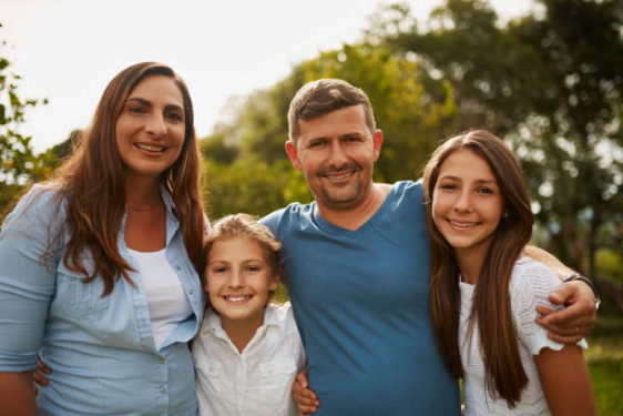 Family of four standing outdoors with arms around each other.